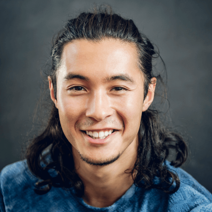 Homem sorridente com cabelo longo, usando uma camisa azul, transmitindo felicidade e confiança.